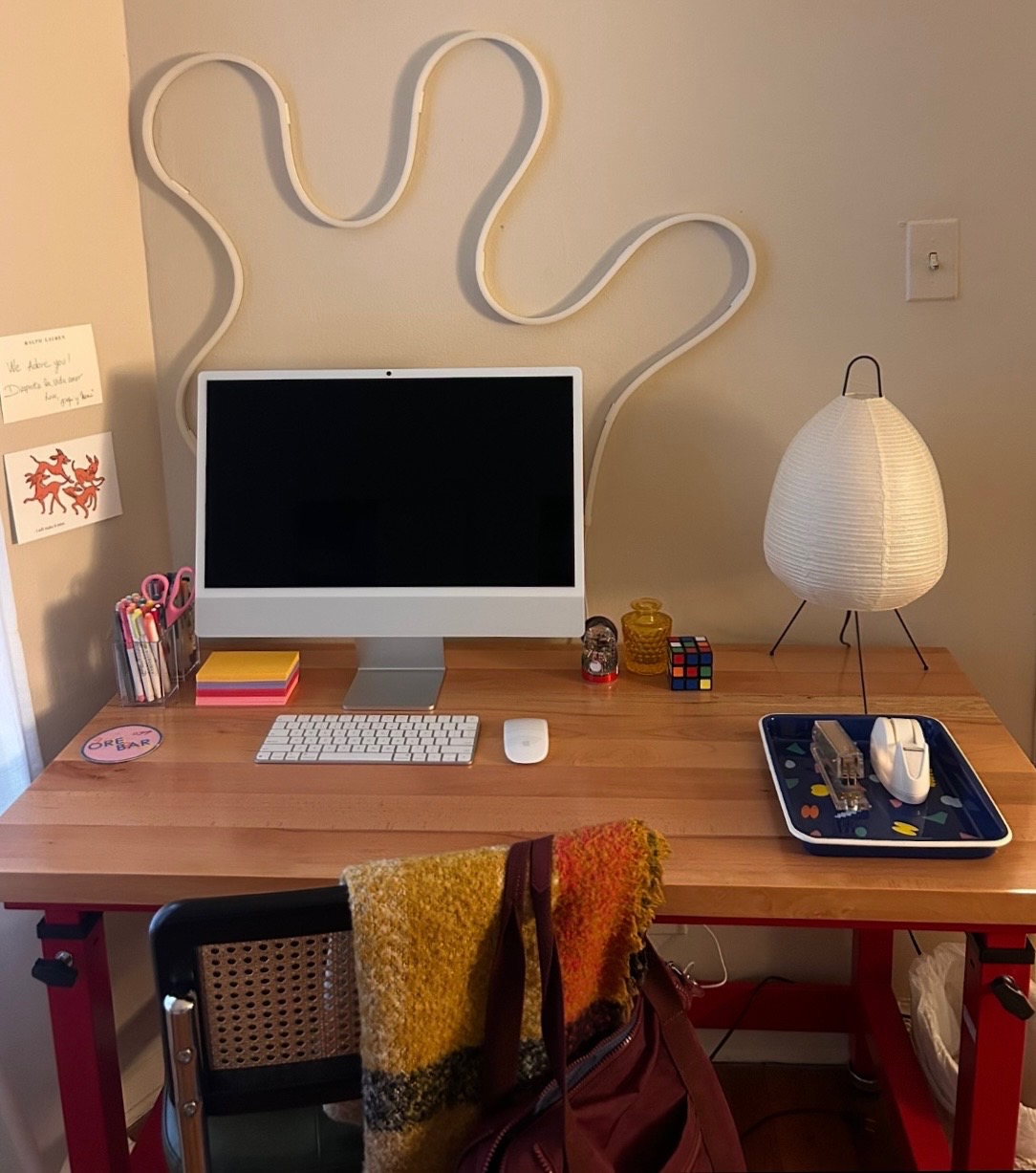A butcher-block workbench desk with red legs, holding a computer, colorful sticky notes, and a paper lamp on it.